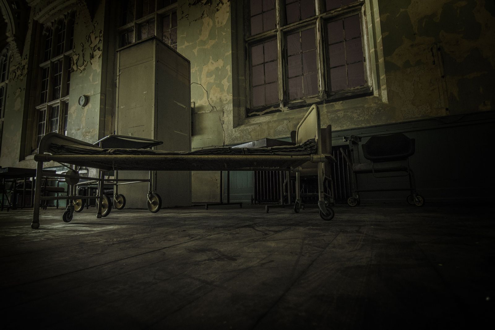 An empty old hospital bed on wheels in a dim, run-down ward